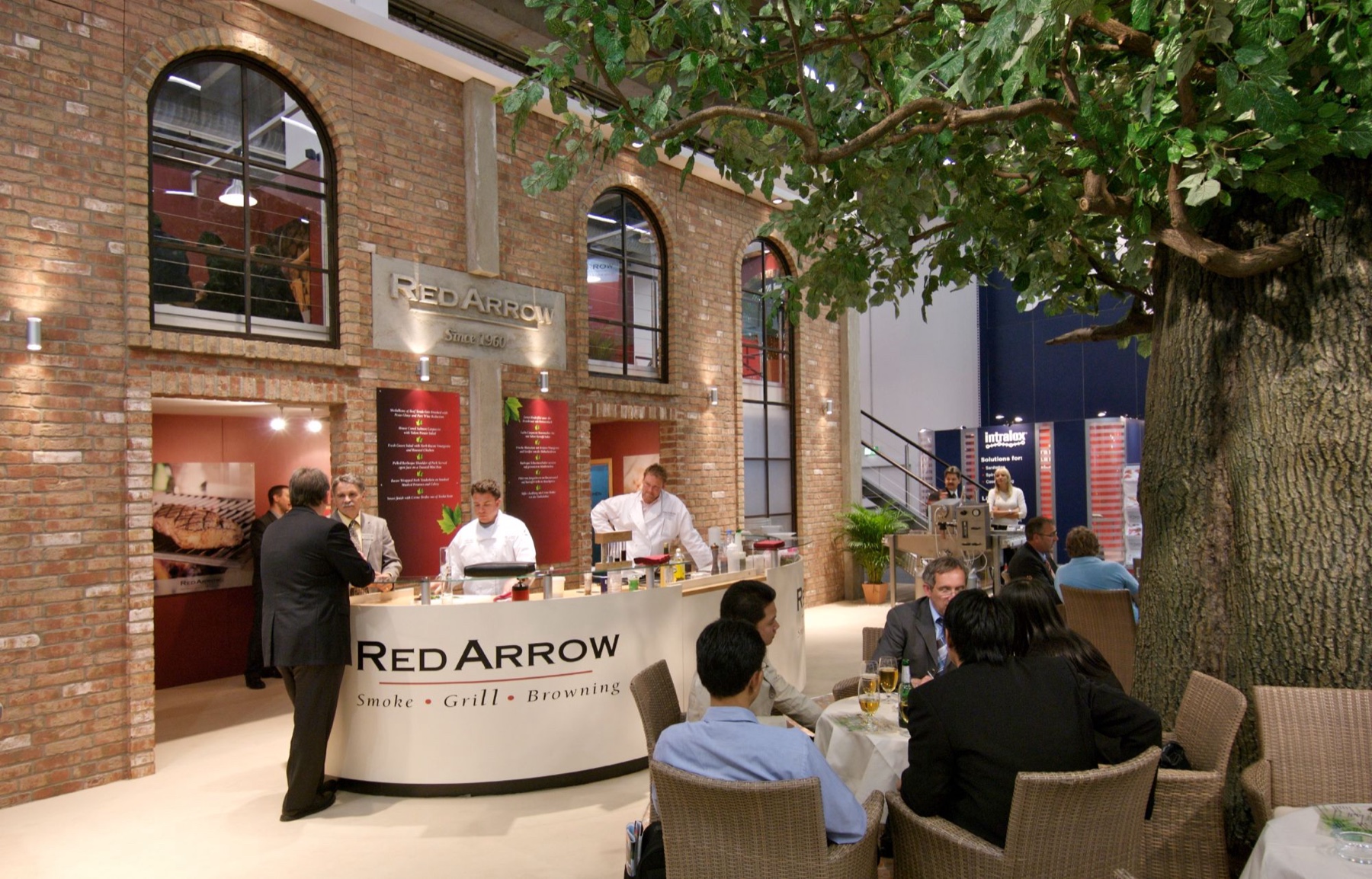 Messestand mit gemauerter Fassade, Rundtresen und großem Baum
